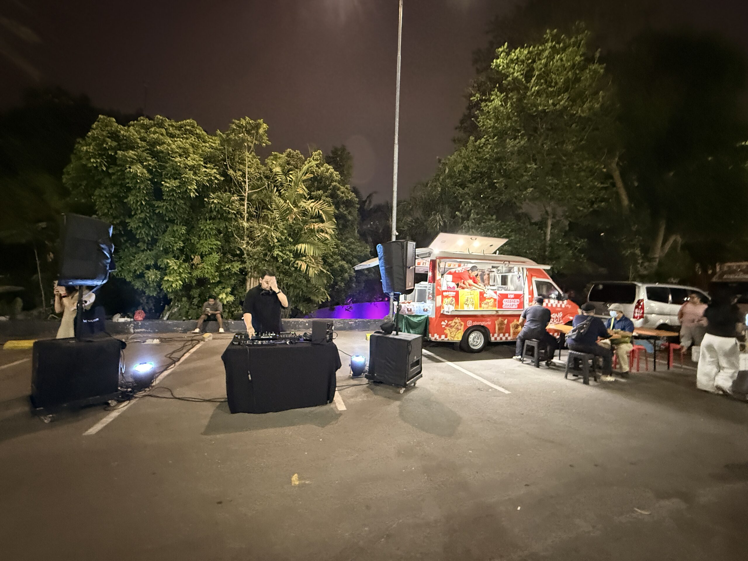 DJ memutar musik di samping truk kebab merah dengan pengunjung di meja panjang